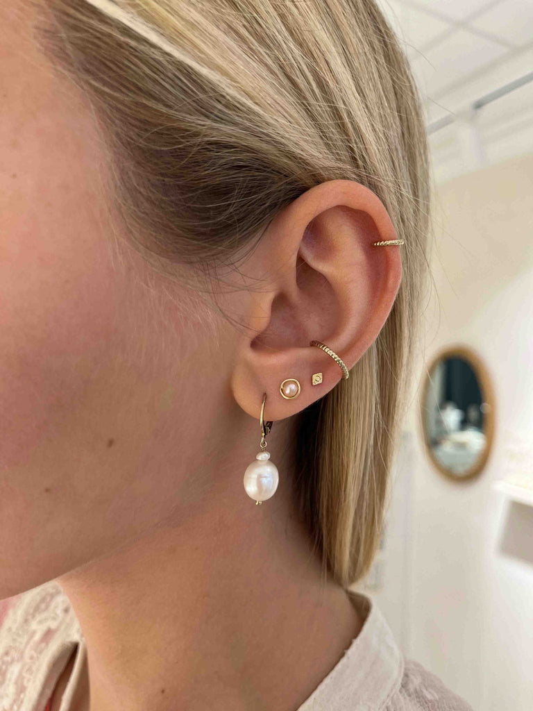 La mannequin porte une boucle d'oreille dorée en perles blanches, une puce d'oreille en gold-filled et perle rose, une mini puce d'oreille losange et deux faux piercings